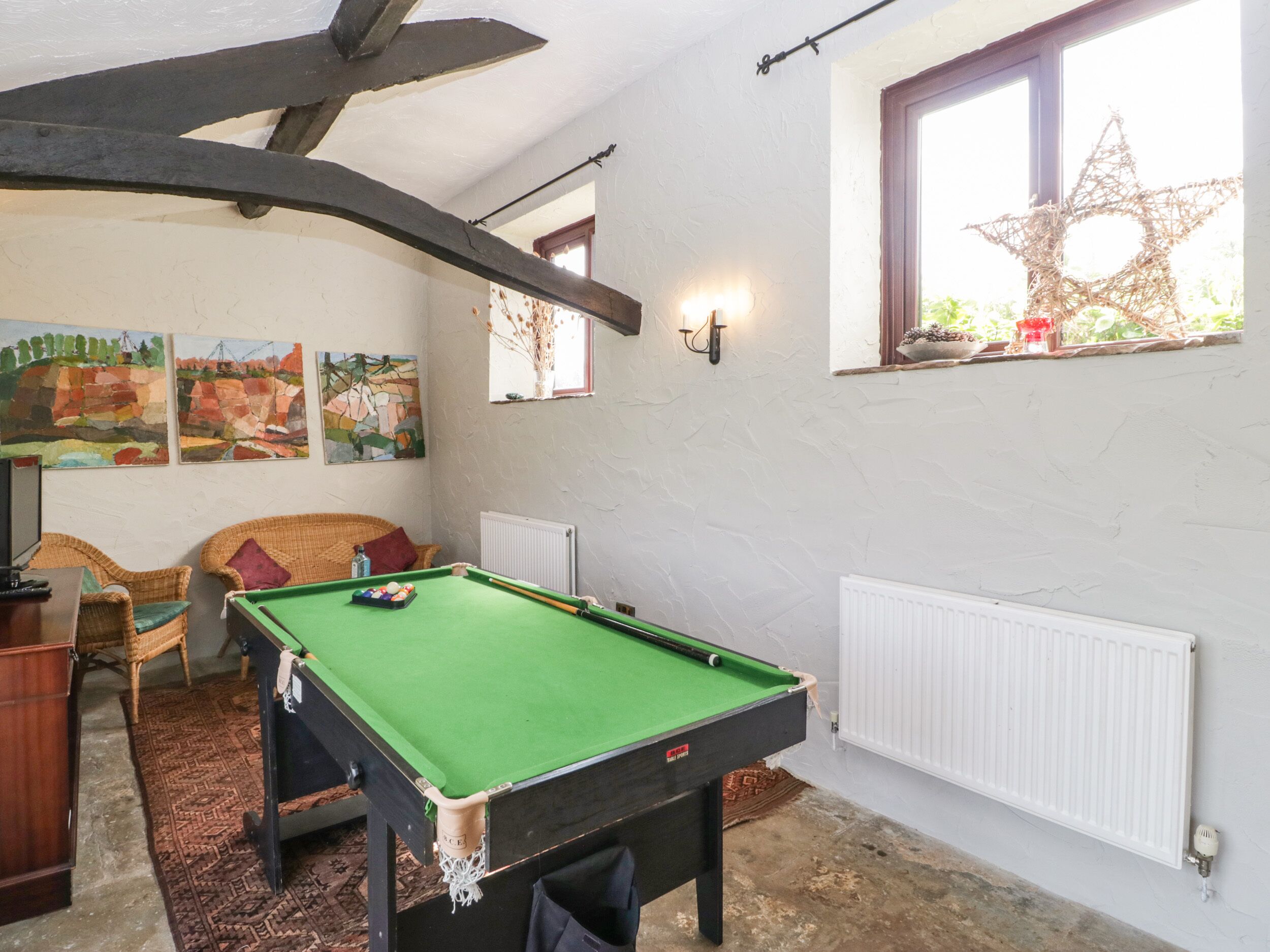 Une pièce chaleureuse avec une table de billard, des meubles en osier et des œuvres d’art accrochées aux murs.
