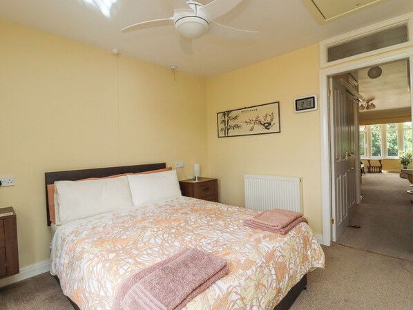 Une chambre à coucher comprenant un lit, une table de chevet, une horloge murale, un radiateur et une porte donnant sur une autre pièce.