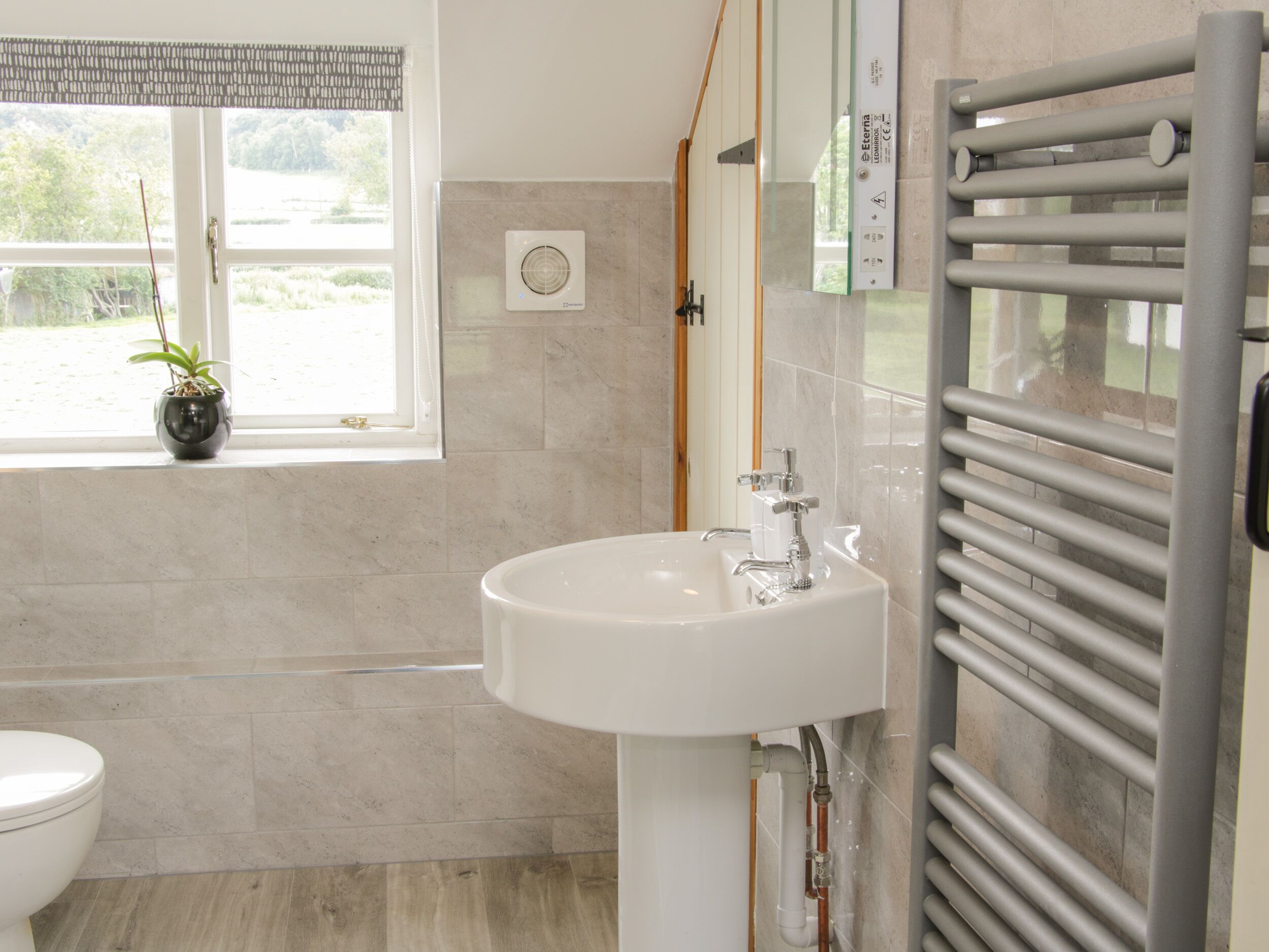 A bathroom with a white sink, a toilet, and a window with a view of greenery.