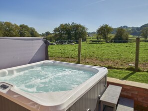 A hot tub with a wooden deck and a brick wall, overlooking a grassy field with cows and trees. - Conquer Hall (Montgomery)