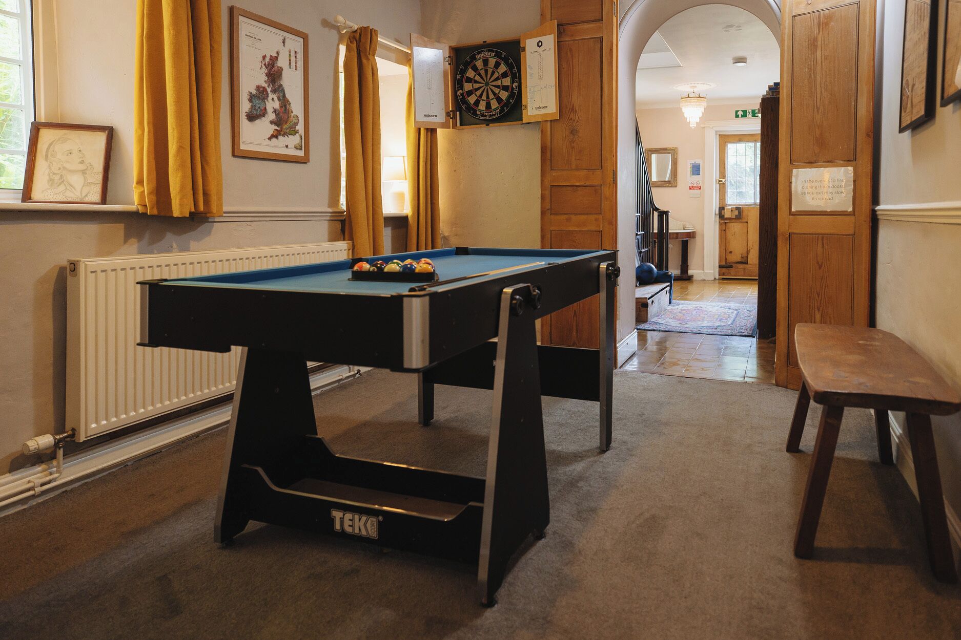 A pool table with balls, a dartboard, and a framed map on the wall.