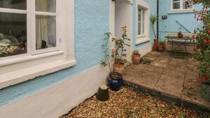 A blue house with a white window, a small porch, and a garden area with potted plants and a table. - Pant y Ffynnon (Haverfordwest)
