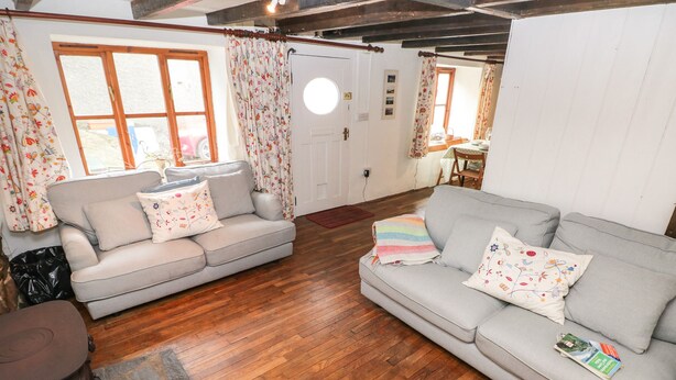 A cozy living room with two grey sofas, floral curtains, and a wooden floor. - Pant y Ffynnon (Haverfordwest)