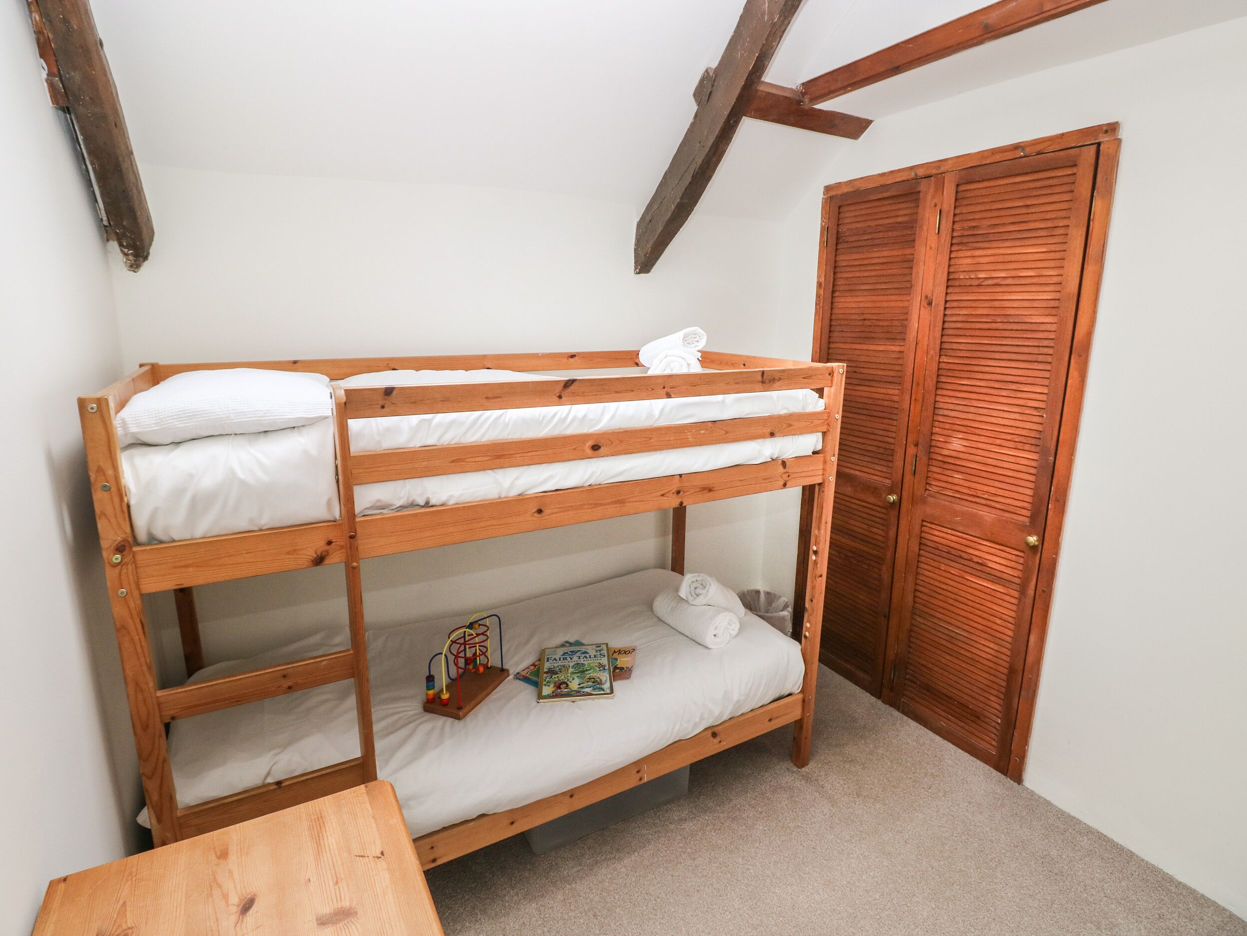 A bunk bed with white bedding, a small table, and a door with louvered panels.