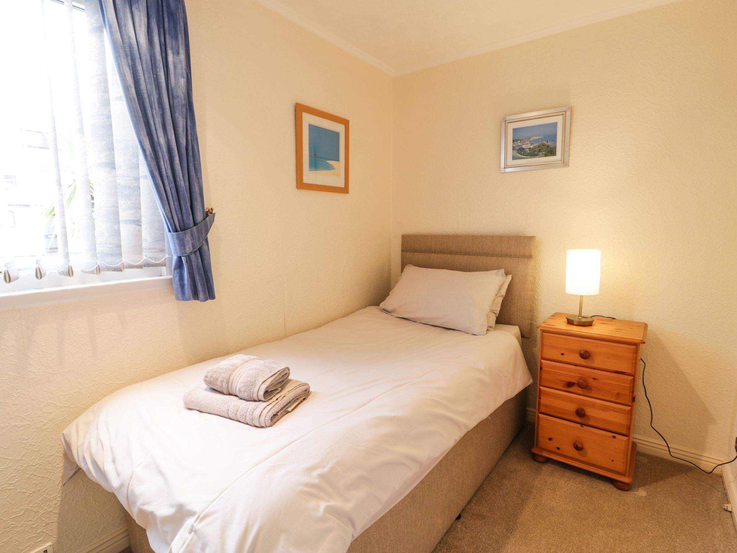 A neatly made bed with a folded towel, a bedside table with a lamp, and two framed pictures on the wall.