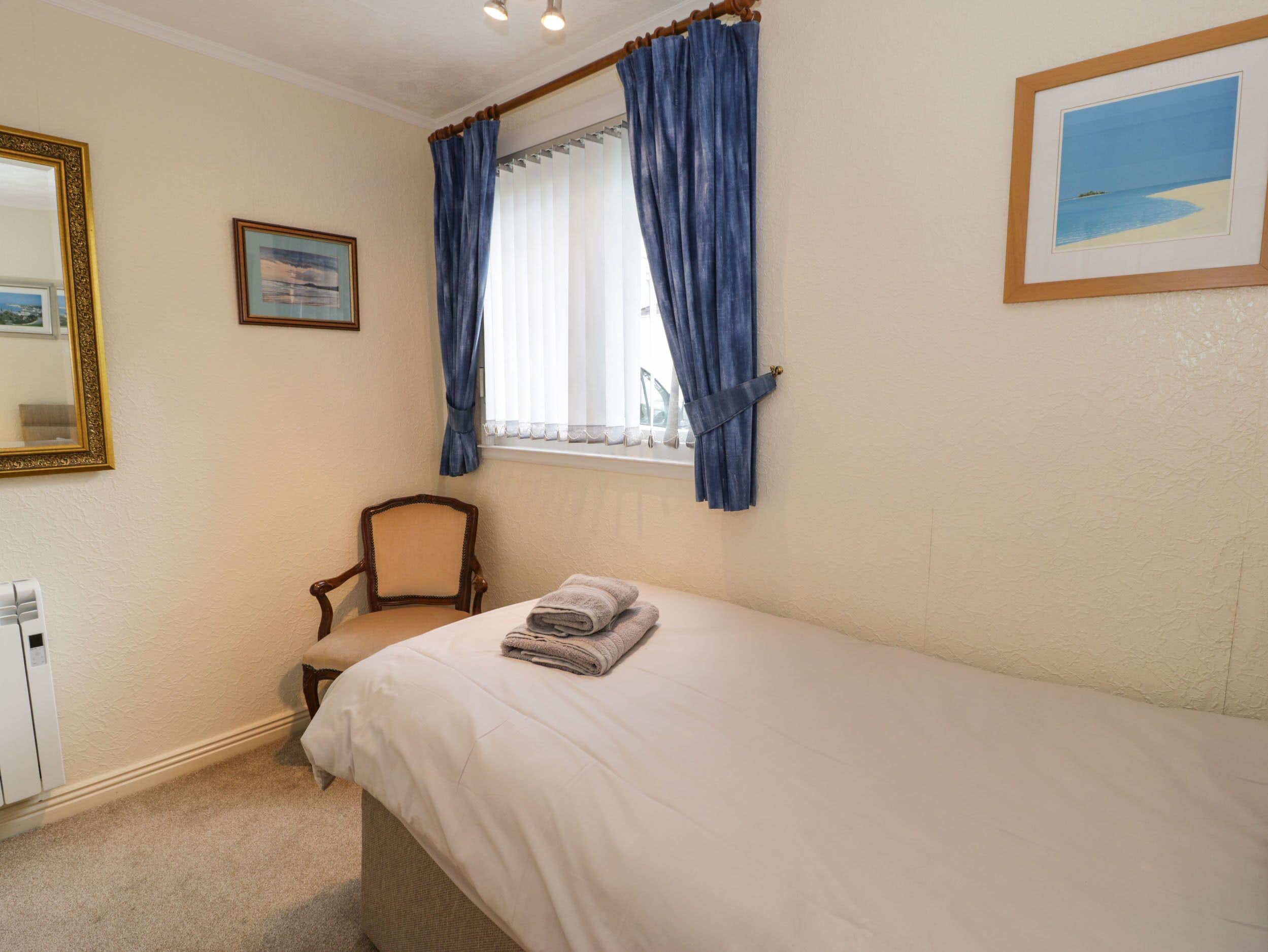 A bedroom with a bed, a chair, a window with curtains, a radiator, and a framed picture on the wall.