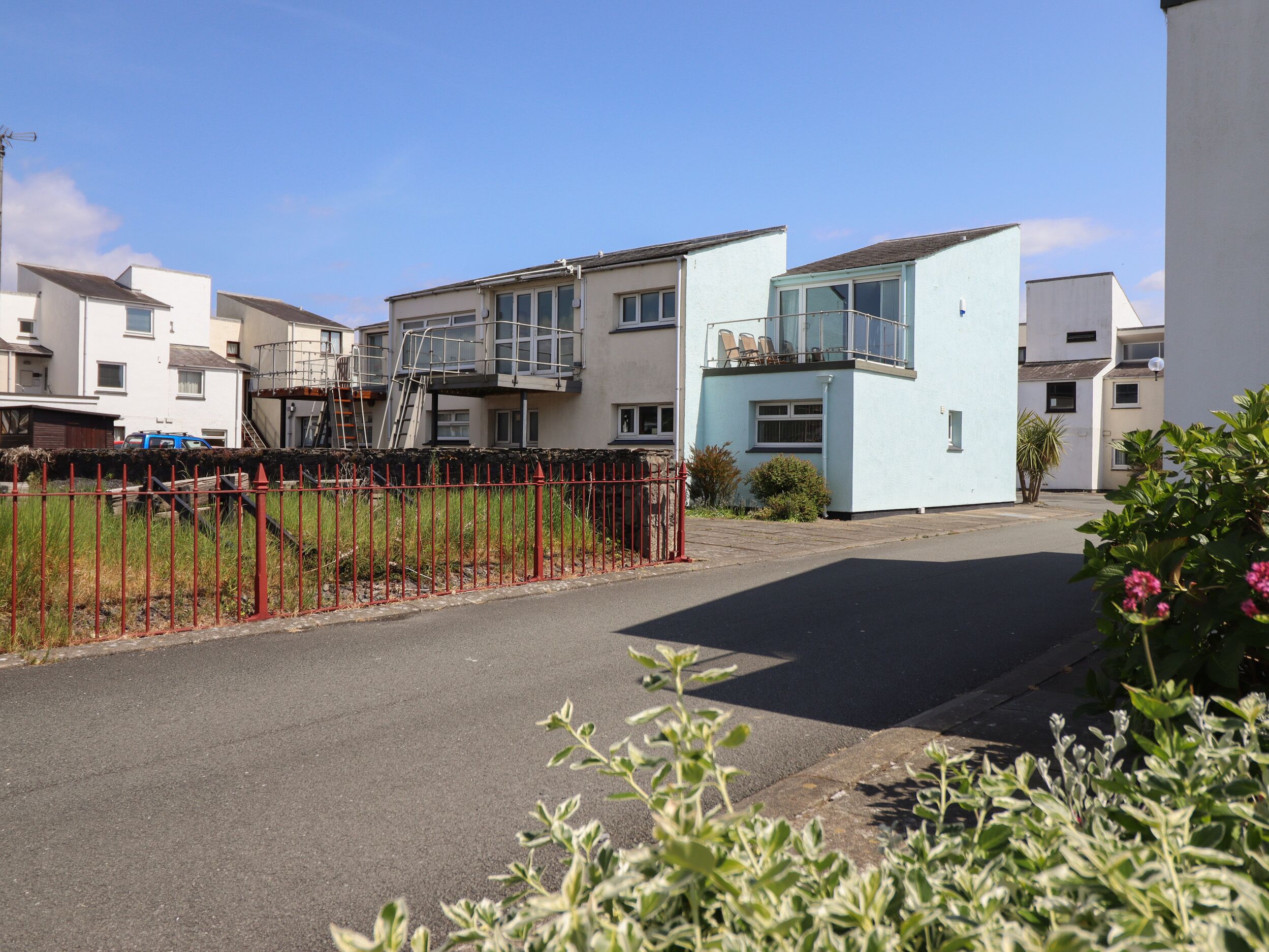 A residential street with houses, a red fence, and a clear sky.