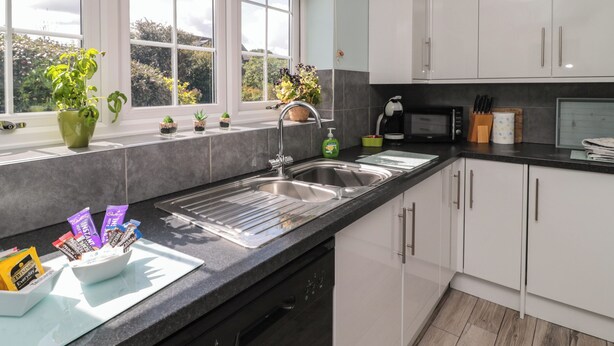 A modern kitchen with a large window, a sink, and a dishwasher. - Island View Cottage (Morpeth)