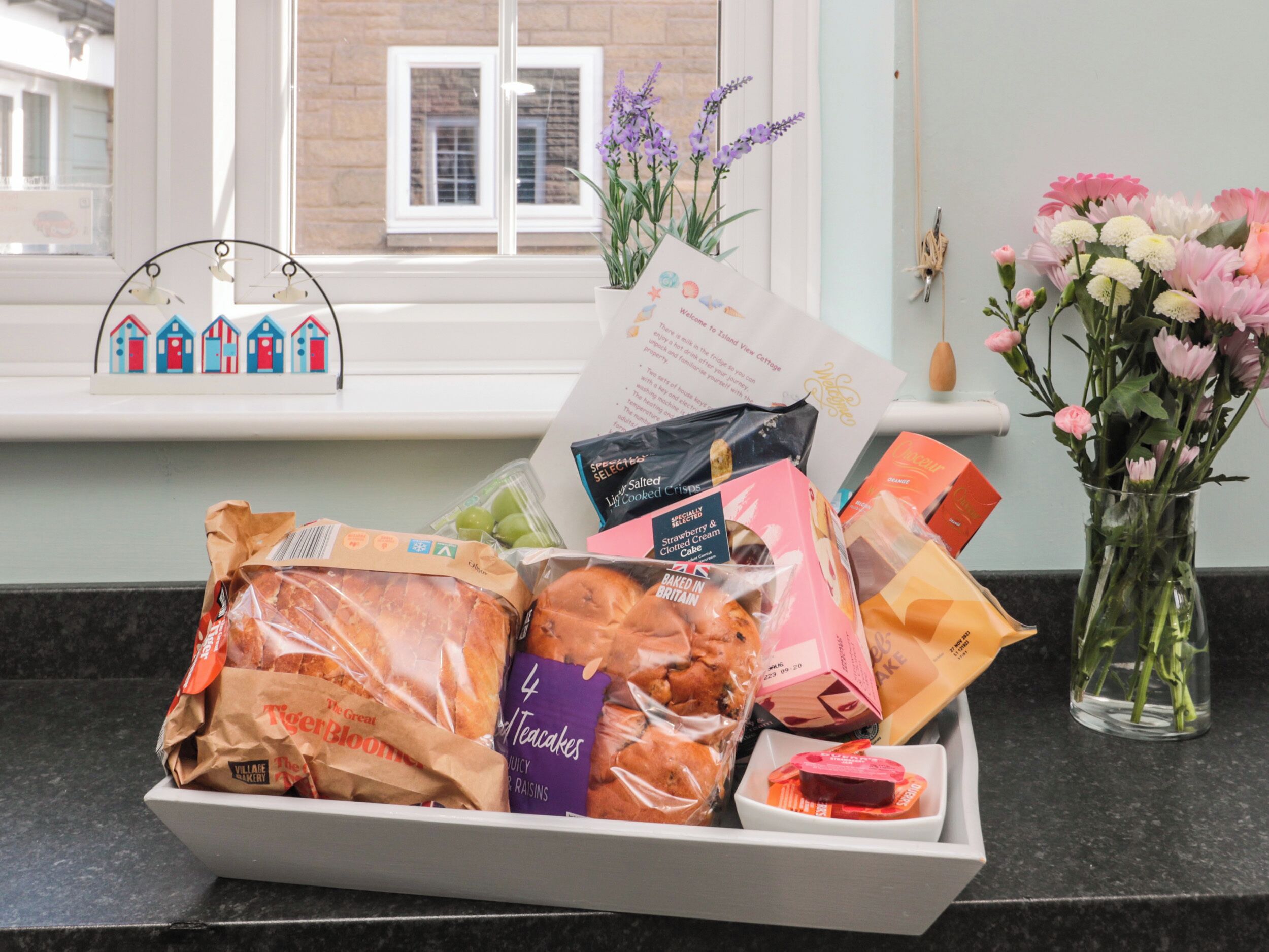 A kitchen counter with a tray of bakery items, a vase of flowers, and a window with a view of buildings.