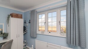 A bedroom with a bed, a desk, a wardrobe, and a window with curtains. - Island View Cottage (Morpeth)