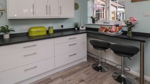 A modern kitchen with white cabinets, a black countertop, and two bar stools. - Island View Cottage (Morpeth)