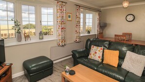 A living room with a leather sofa, a wooden coffee table, and a TV on a stand. - Island View Cottage (Morpeth)