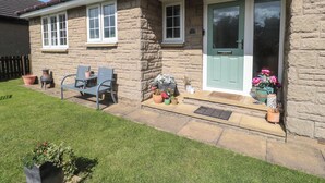 A stone house with a green door, a small porch, and a seating area with chairs and potted plants. - Island View Cottage (Morpeth)