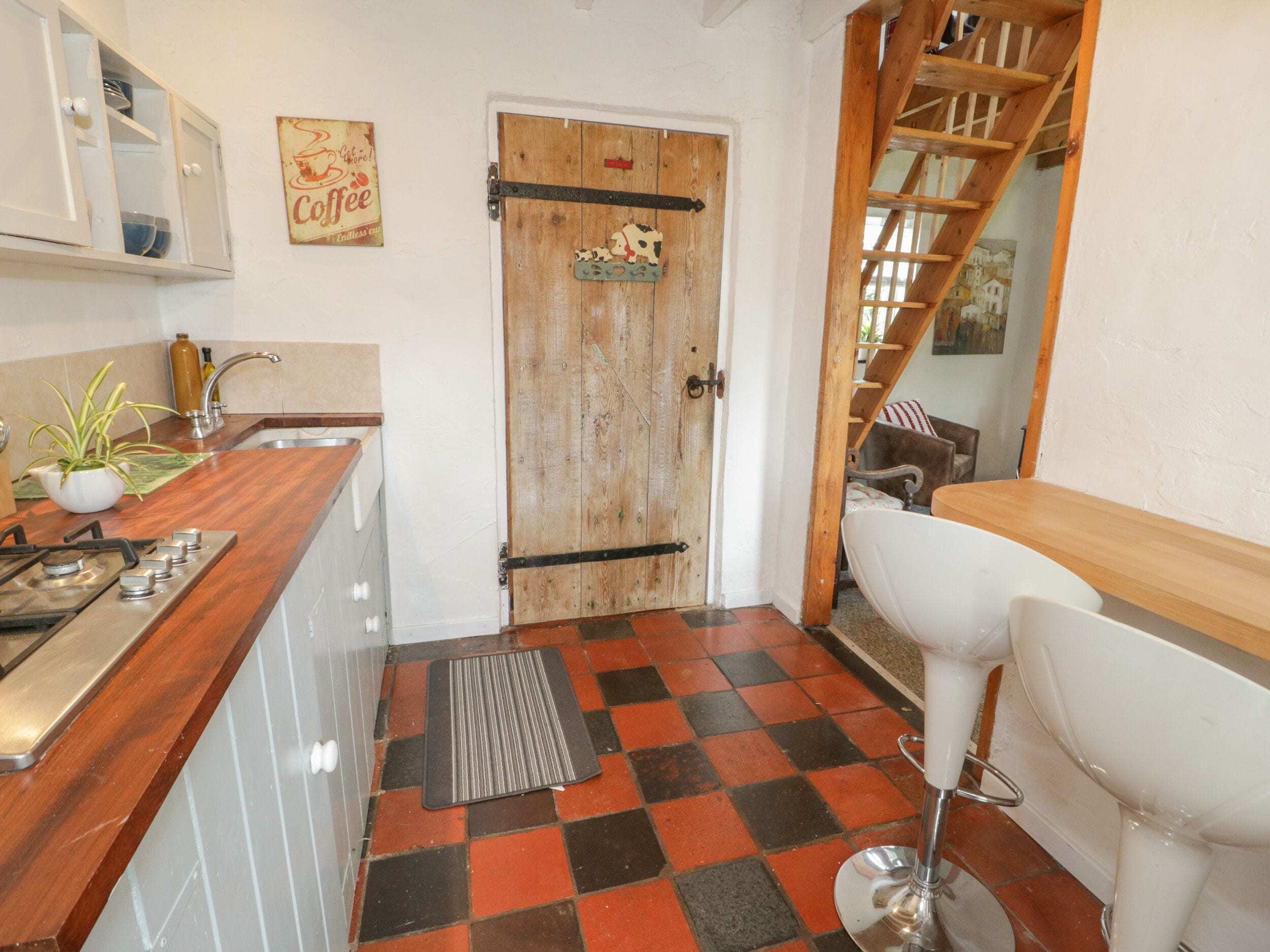 A kitchen with a wooden door, a tiled floor, a stove, and a sink.
