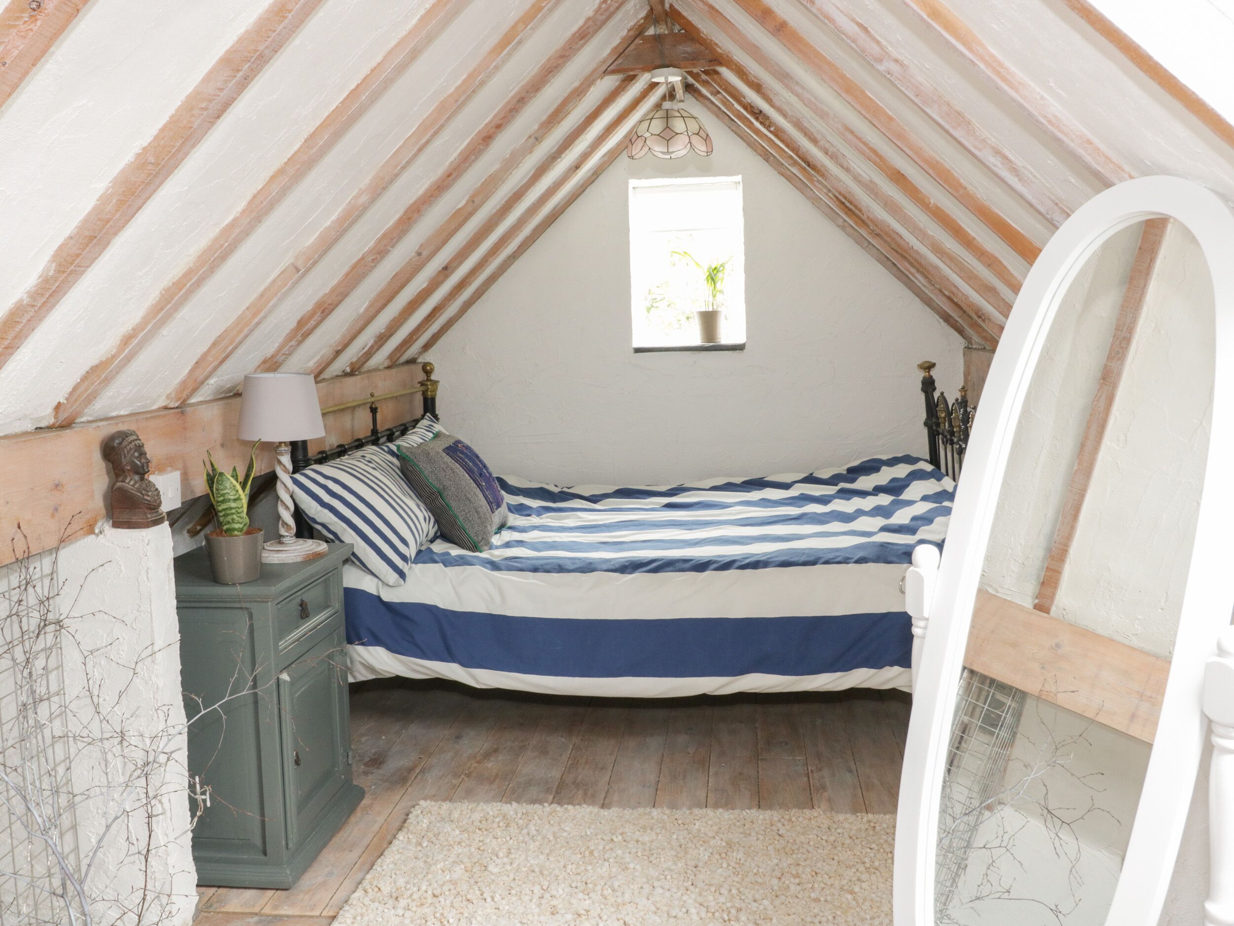 Ein gemütliches Schlafzimmer im Dachgeschoss mit Bett, Nachttisch, Lampe und kleinem Fenster.