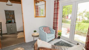 Een gezellige woonkamer met een blauwe fauteuil, een bruine leren bank, een klein bijzettafeltje met een plant en uitzicht op een tuin door een glazen deur.