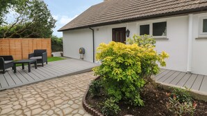 A house with a tiled roof, a wooden deck, and a garden with yellow flowers. - Little Valley View (Hayle)