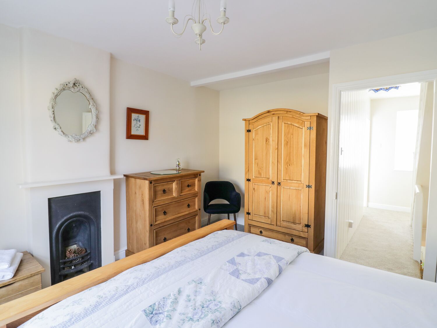 Un dormitorio con cama, armario de madera, silla, chimenea y espejo en la pared.