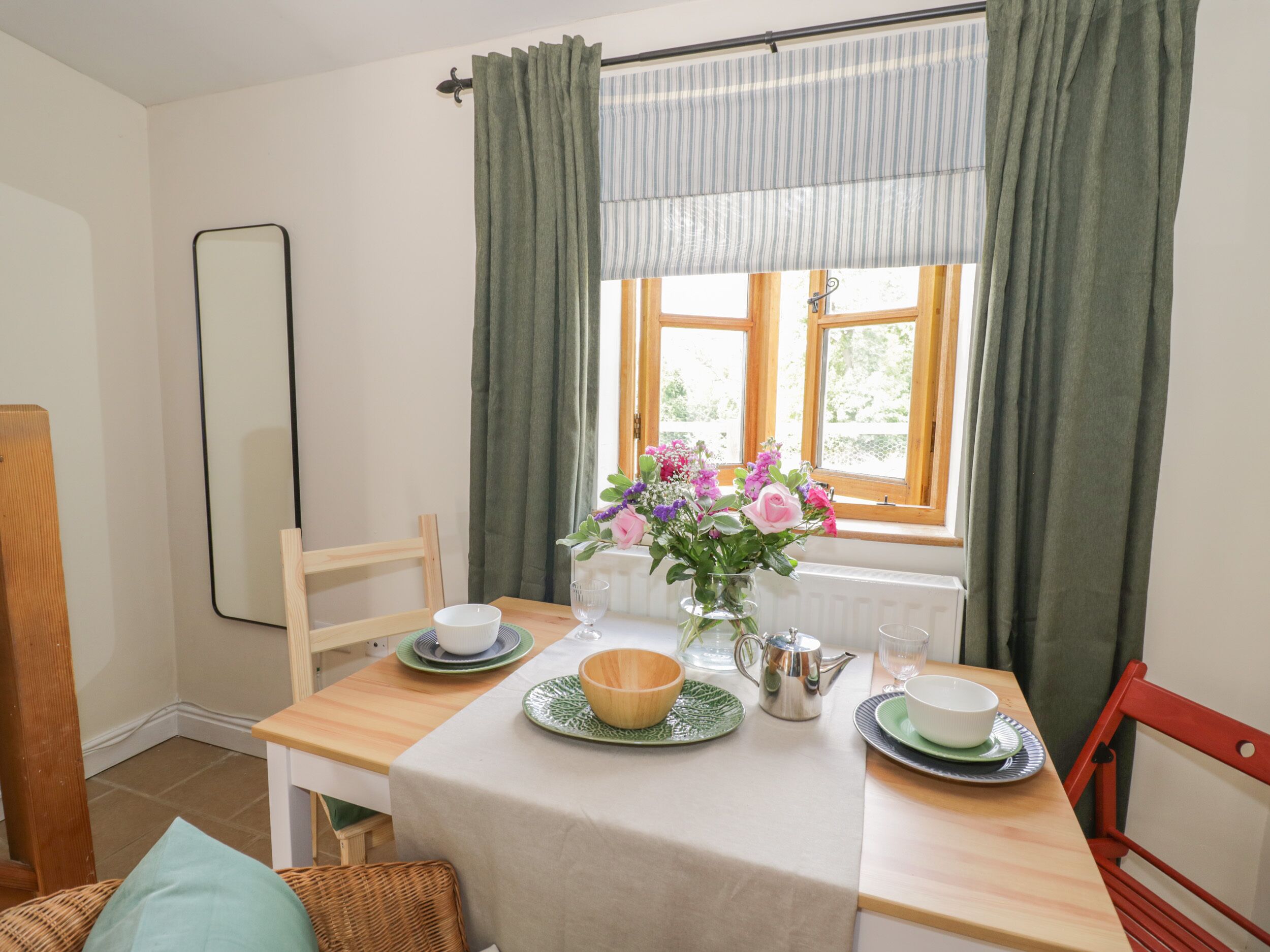 En matplats med ett bord dukat för två personer, en vas med blommor och ett fönster med gardiner.