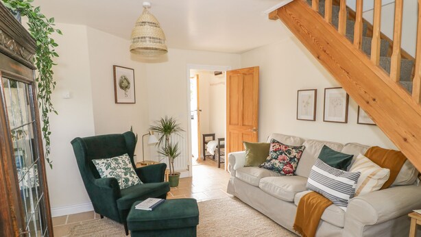 A cozy living room with a green armchair, a beige sofa, and a wooden staircase.
