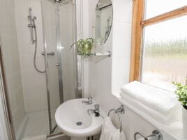 Un baño con ducha acristalada, lavamanos blanco y ventana.