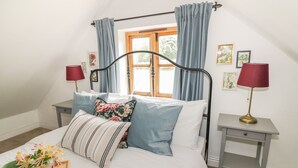 A bedroom with a bed, two bedside tables, a window with curtains, and a lamp.