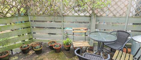 A patio area with a wooden fence, potted plants, a bench, and a table with chairs.