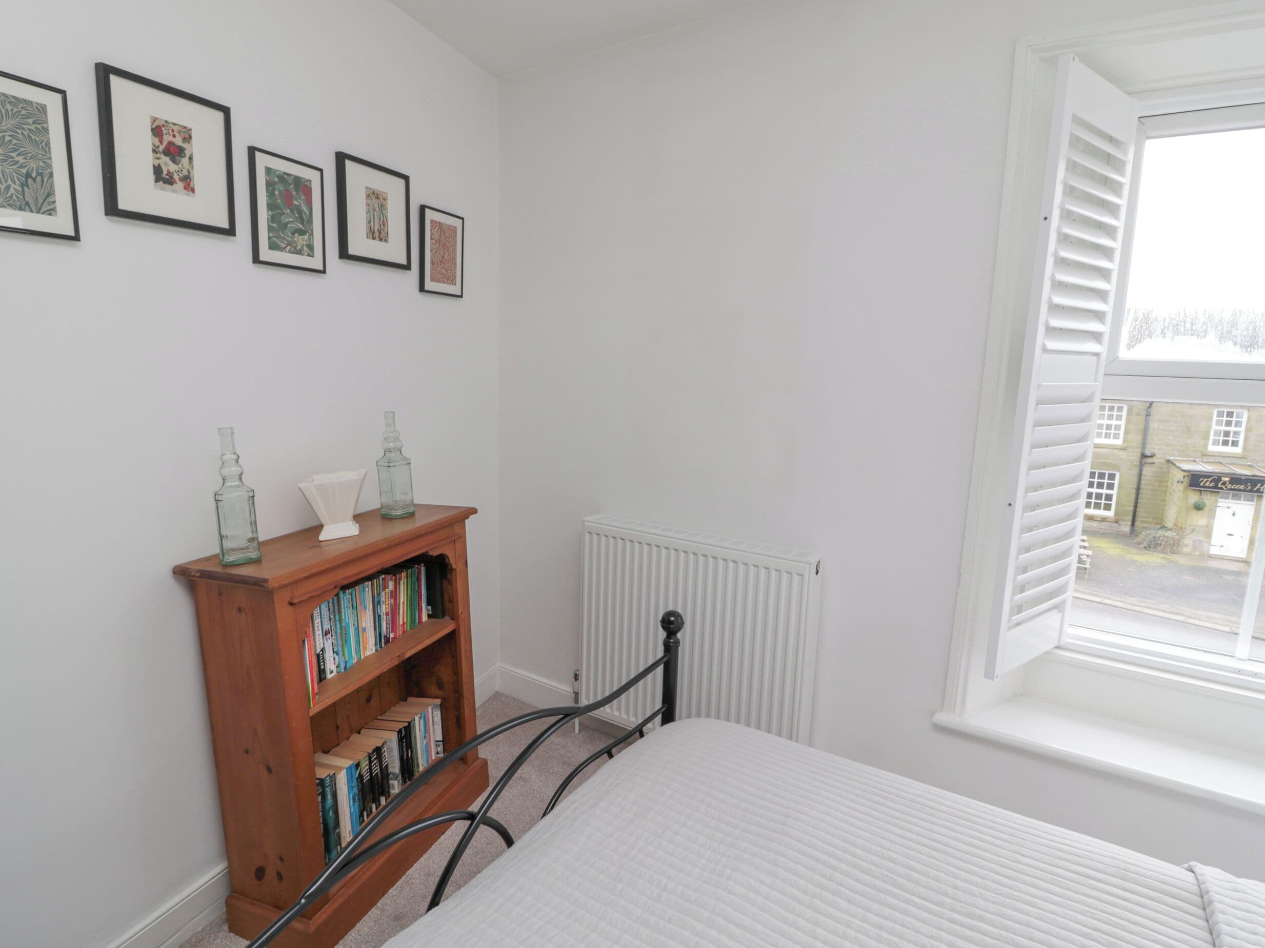 A bedroom with a bed, a wooden bookshelf, a radiator, and a window with shutters.