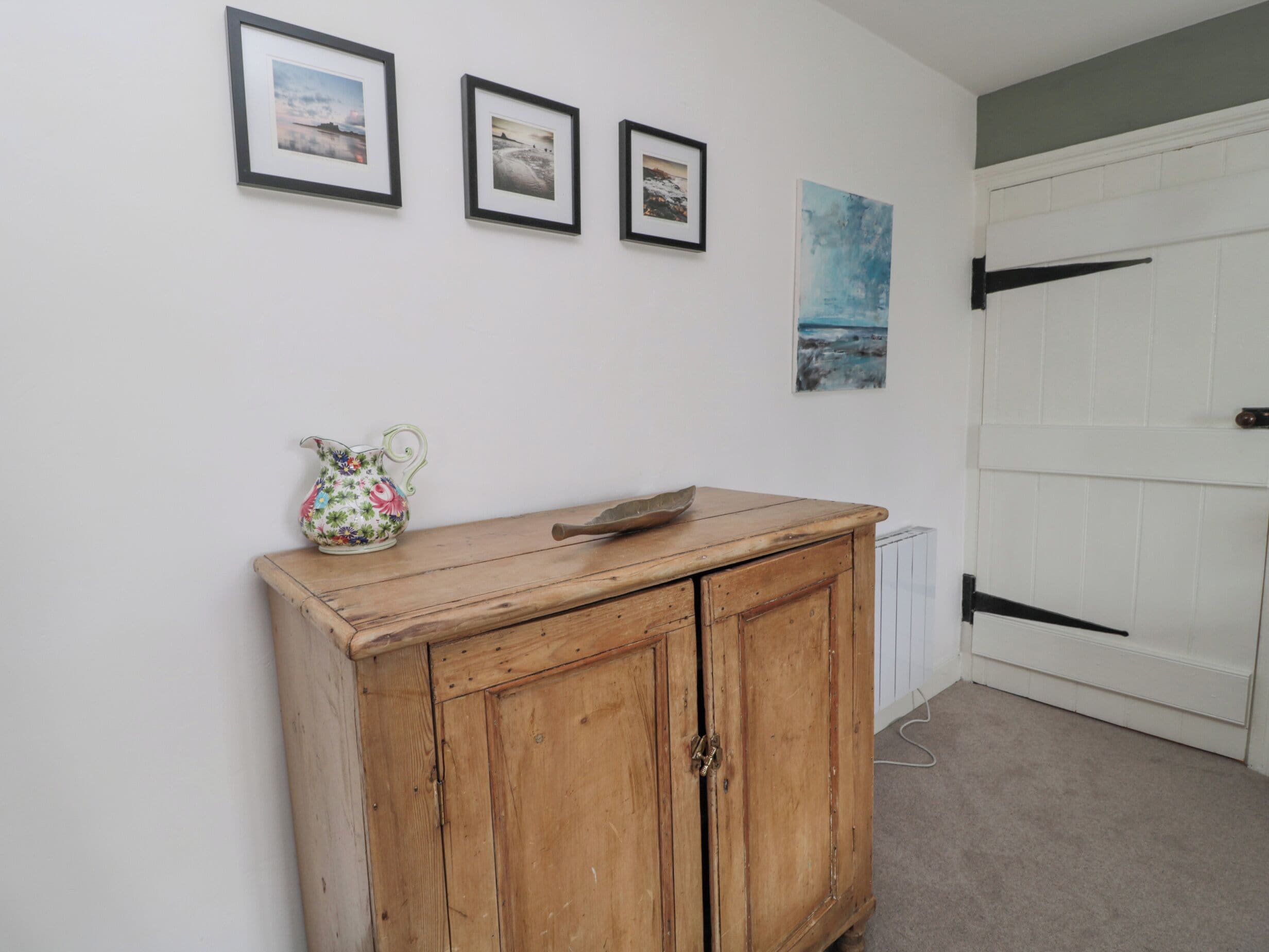 Een kamer met een houten kast, een radiator en drie ingelijste foto’s aan de muur.