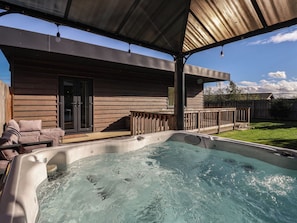 Un jacuzzi bajo un porche cubierto, con una casa de madera al fondo.