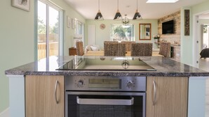 Una cocina con encimeras de granito, electrodomésticos de acero inoxidable y un horno empotrado. Cuenta con una zona de estar con cojines estampados y un televisor montado en la pared.