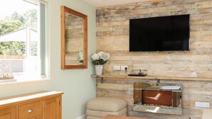 Una sala de estar con una pared de madera, un televisor de pantalla plana, un mueble de madera, un sofá color beige y una pequeña mesa.