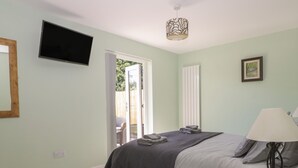 Un dormitorio con cama, televisión, lámpara de noche, control remoto y ventana con vistas al exterior.