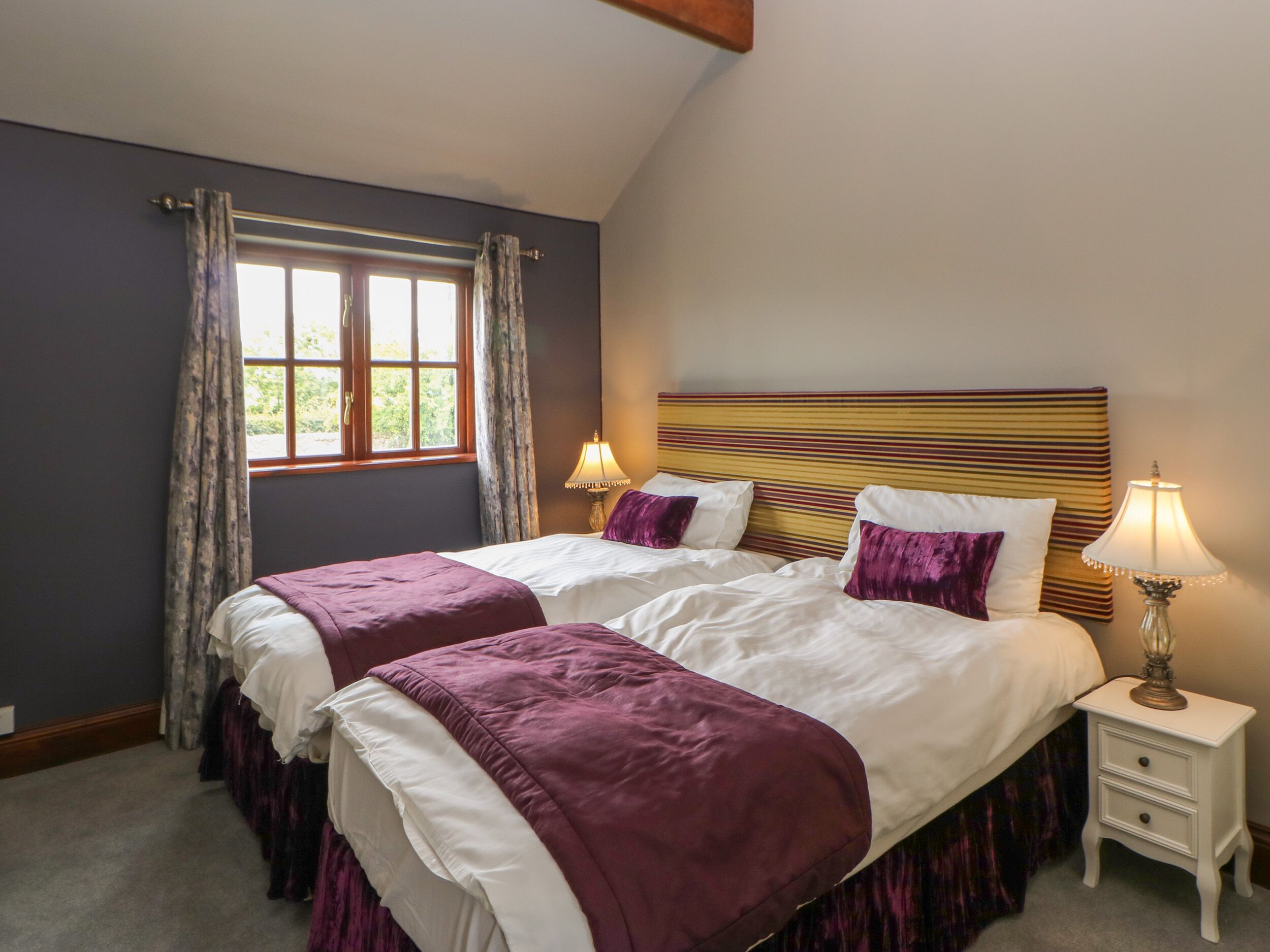 A double bed with a striped headboard, two bedside tables, and a window with curtains.