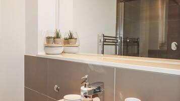 A modern bathroom with a large mirror, a sink with a chrome faucet, and two small potted plants on the countertop.