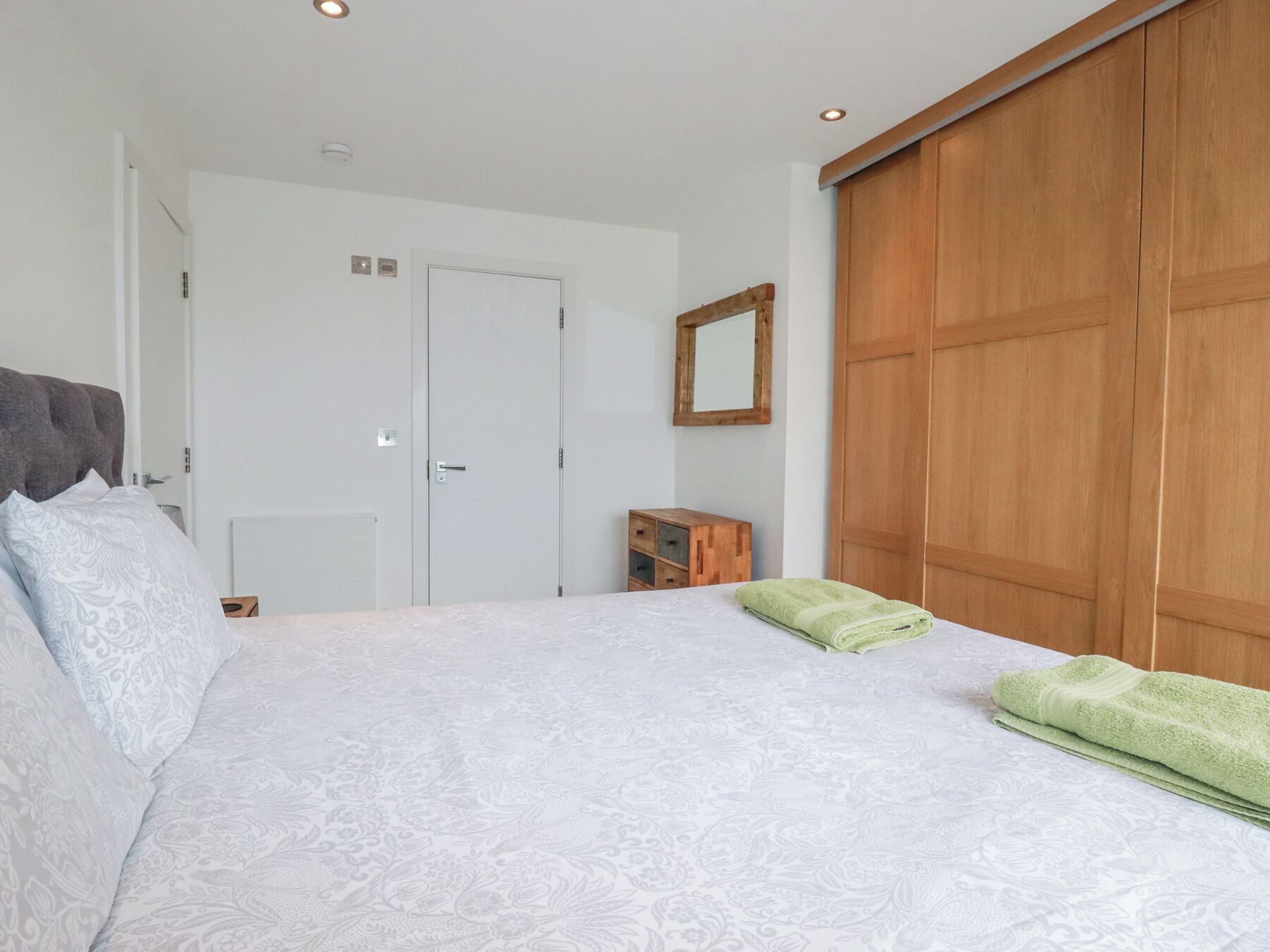 Un dormitorio con una cama, un armario de madera, un espejo y un mueble de madera.
