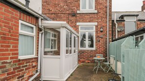 A brick house with a white door and windows, a small patio with a table and chairs, and a green fence. - Mulgrave Cottage (Saltburn-by-the-Sea)