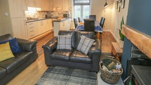 A modern kitchen with wooden cabinets, a dining area with a table and chairs, a leather sofa with cushions, and a fireplace. - Mulgrave Cottage (Saltburn-by-the-Sea)