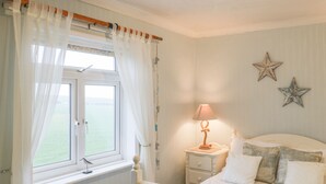A bedroom with a bed, a nightstand with a lamp, a window with curtains, and star decorations on the wall. - Mulgrave Cottage (Saltburn-by-the-Sea)
