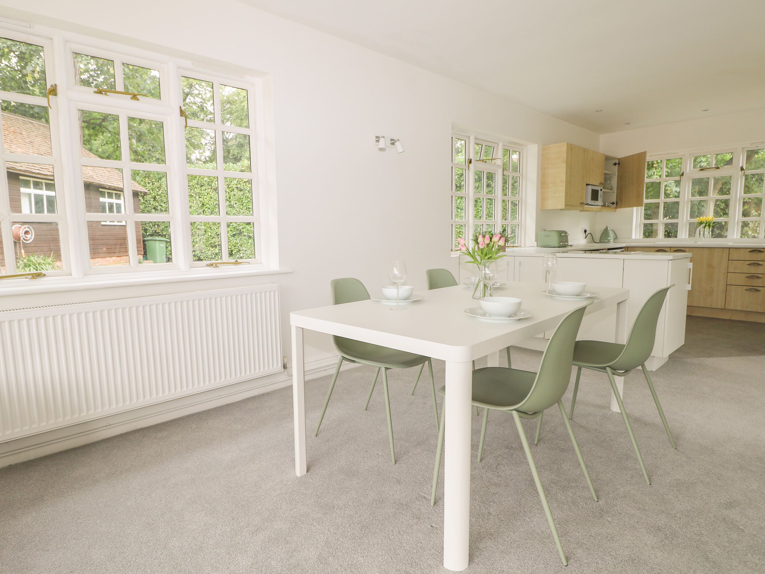 A modern kitchen with white cabinetry, a dining table with chairs, and large windows offering a view of the greenery outside.