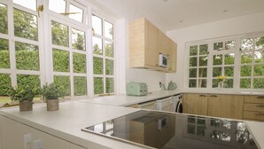 A modern kitchen with a large island, built-in appliances, and large windows offering a view of greenery. - Thames Reach (Wallingford)