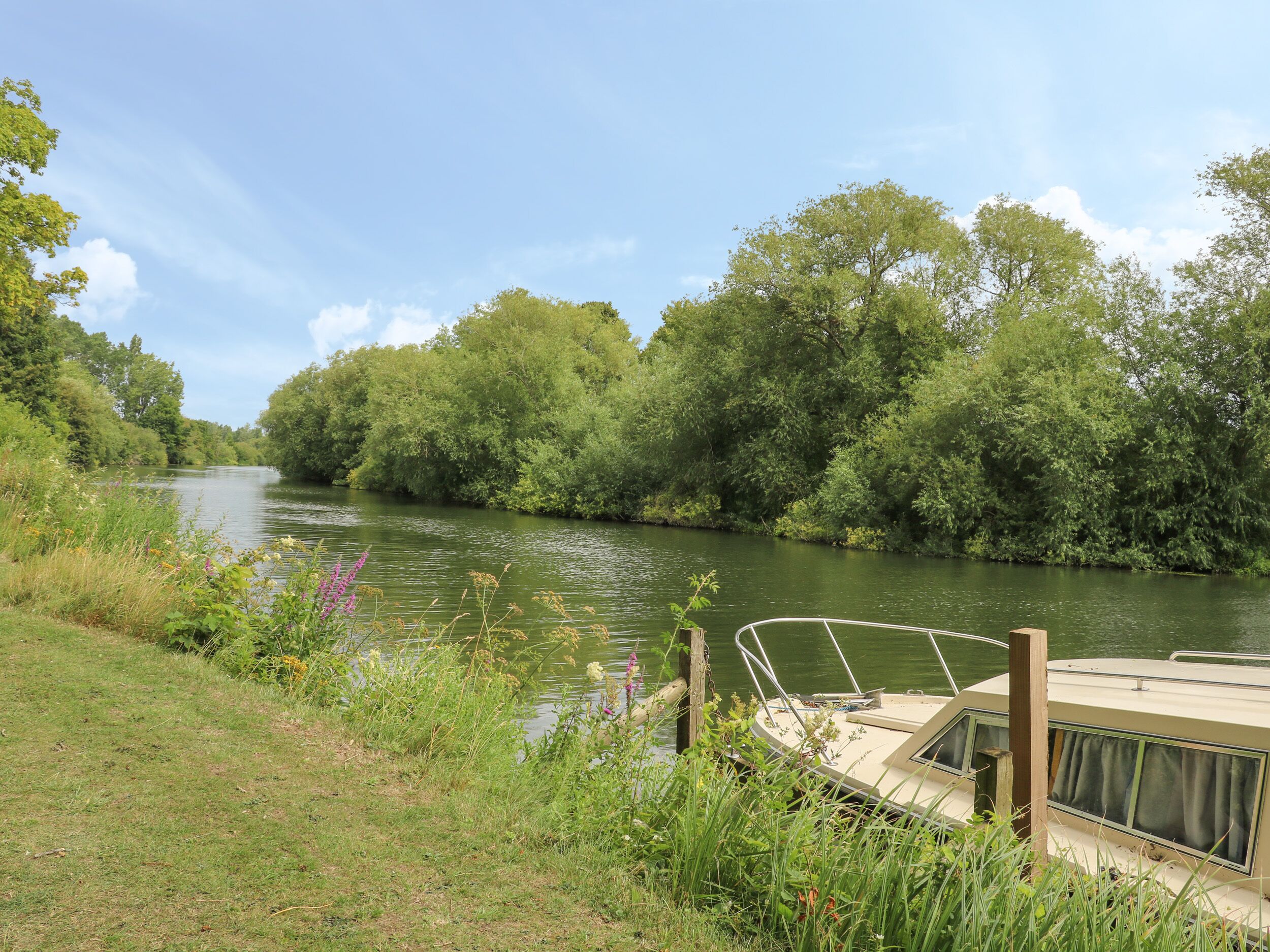 A river with a boat docked on the right, surrounded by lush greenery and trees.