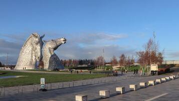 A large metallic sculpture of a horse's head in a public square with a paved walkway and benches.