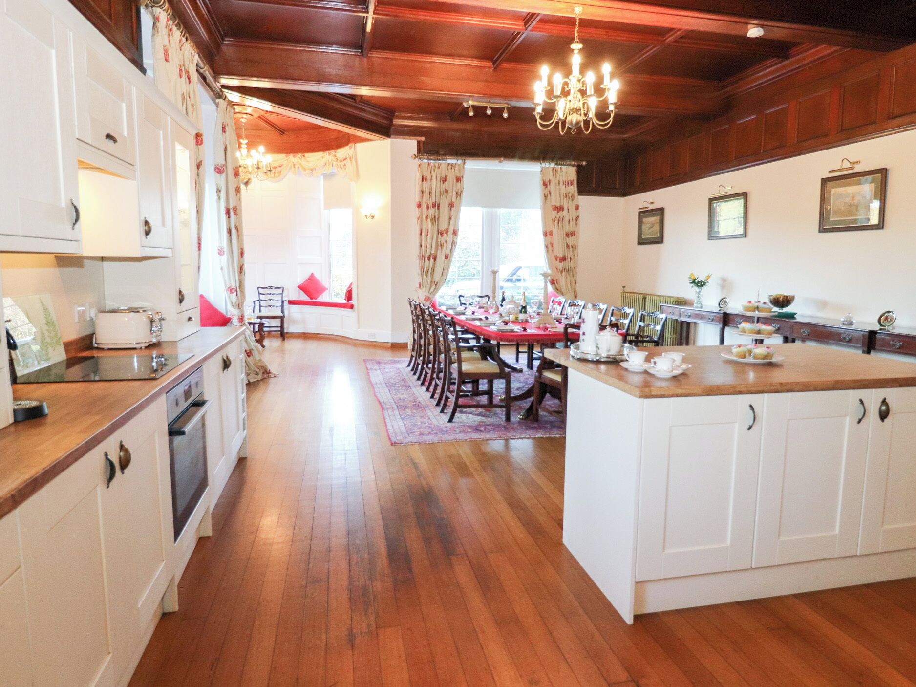Une cuisine spacieuse avec un plancher en bois, des meubles blancs et un coin repas avec une table dressée pour quatre personnes.