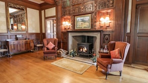 Una habitación amplia con una chimenea grande, dos sillones, un aparador de madera y un candelabro.
