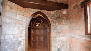 Una entrada de paredes de piedra con una puerta de madera, un pequeño jarrón de flores y un banco de madera.