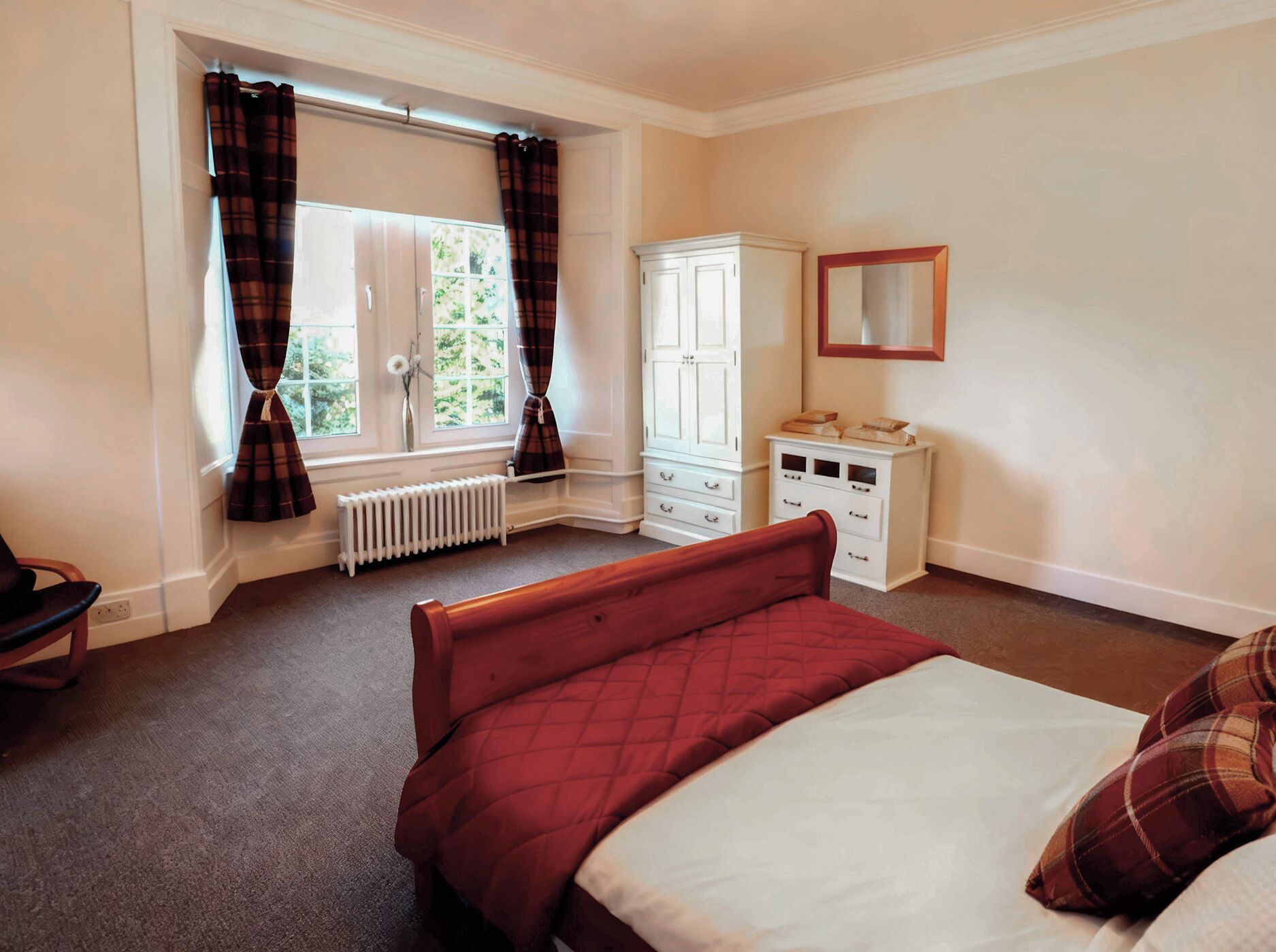 A bedroom with a bed, a wardrobe, a radiator, and a window with curtains.