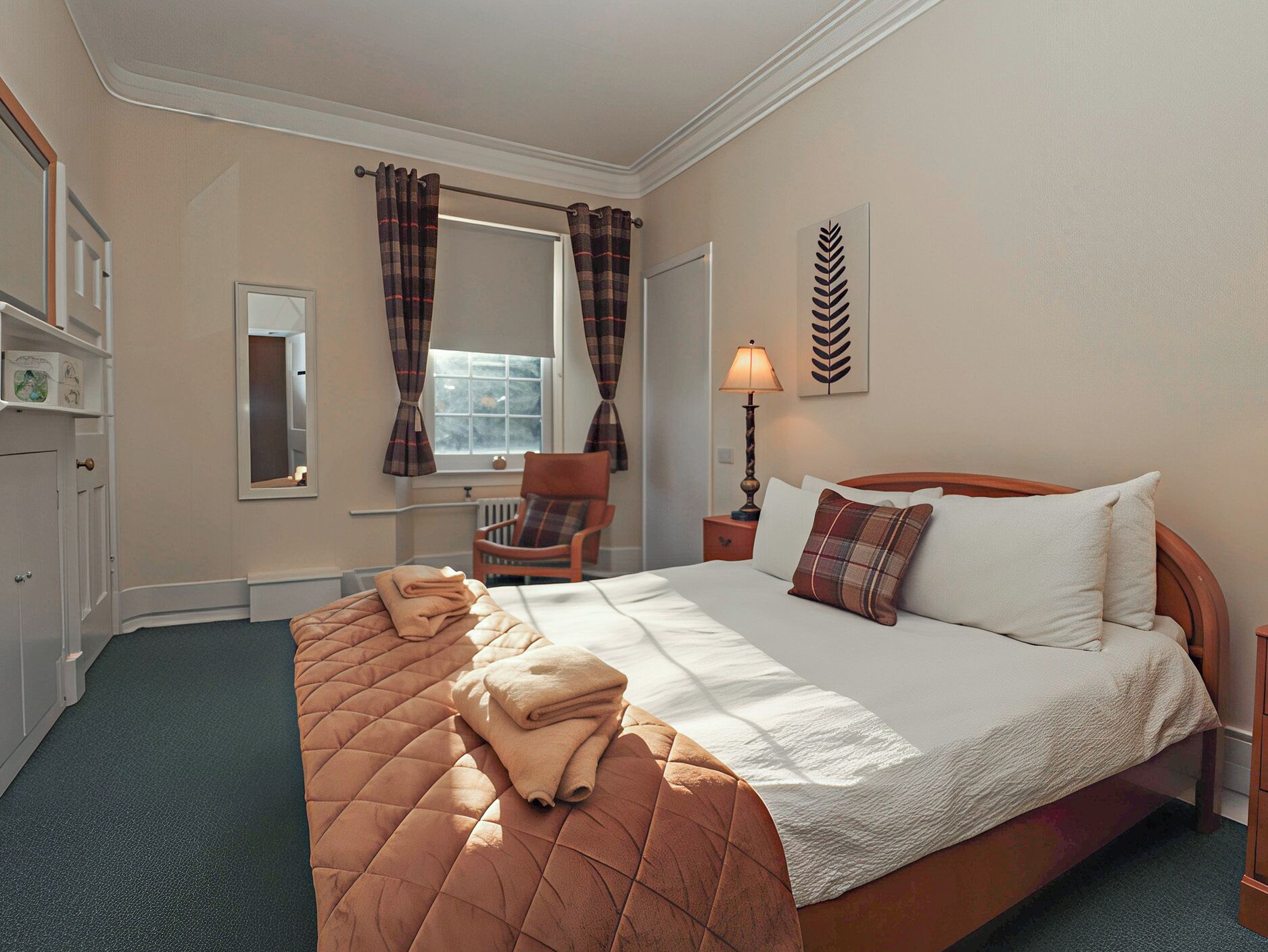 Habitación de hotel con una cama grande, una silla, una mesita de noche con lámpara, una ventana con cortinas y un radiador.