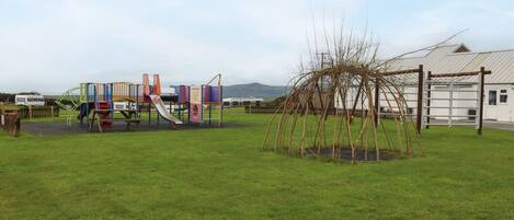 Un parque infantil con juegos de colores y un pequeño árbol en un área verde.