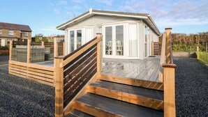 A modern house with a wooden deck and a glass door leading to a covered porch. - Caban Tywod (Pwllheli)